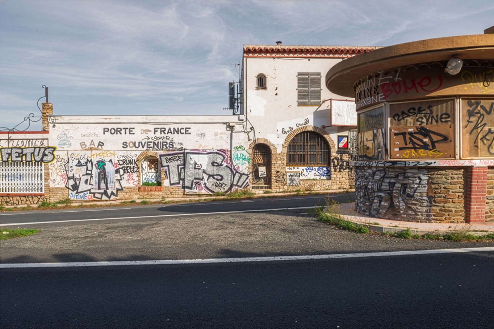 Un edifici abandonat amb 'Porte de France, Souvenirs' escrit a la paret, cobert de grafits davant d'una carretera buida.