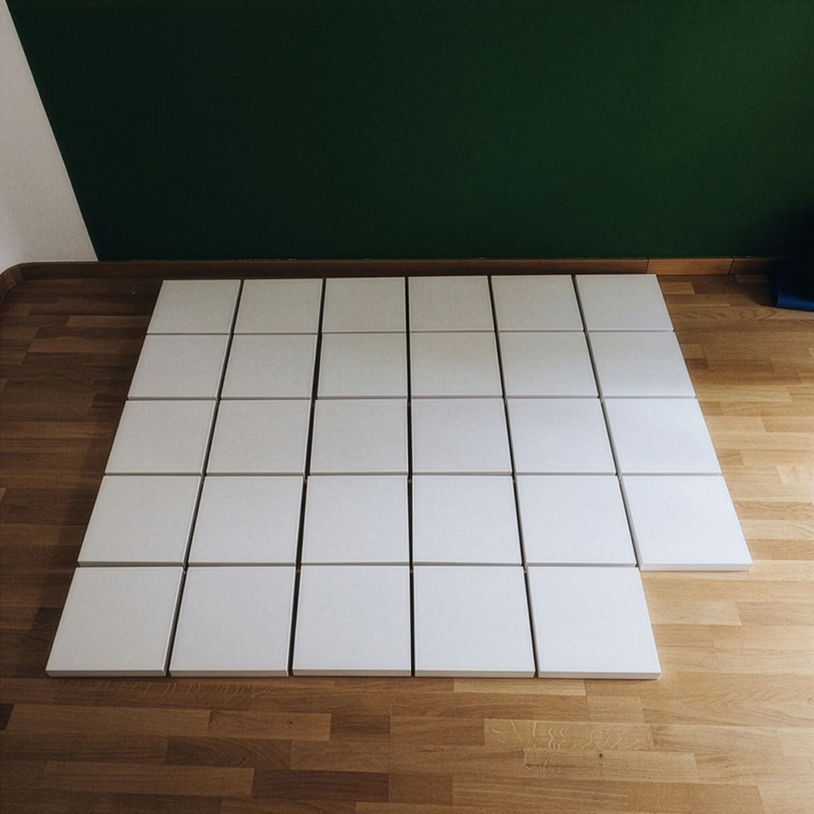 Una cuadrícula de lienzos cuadrados blancos dispuestos en un suelo de madera.