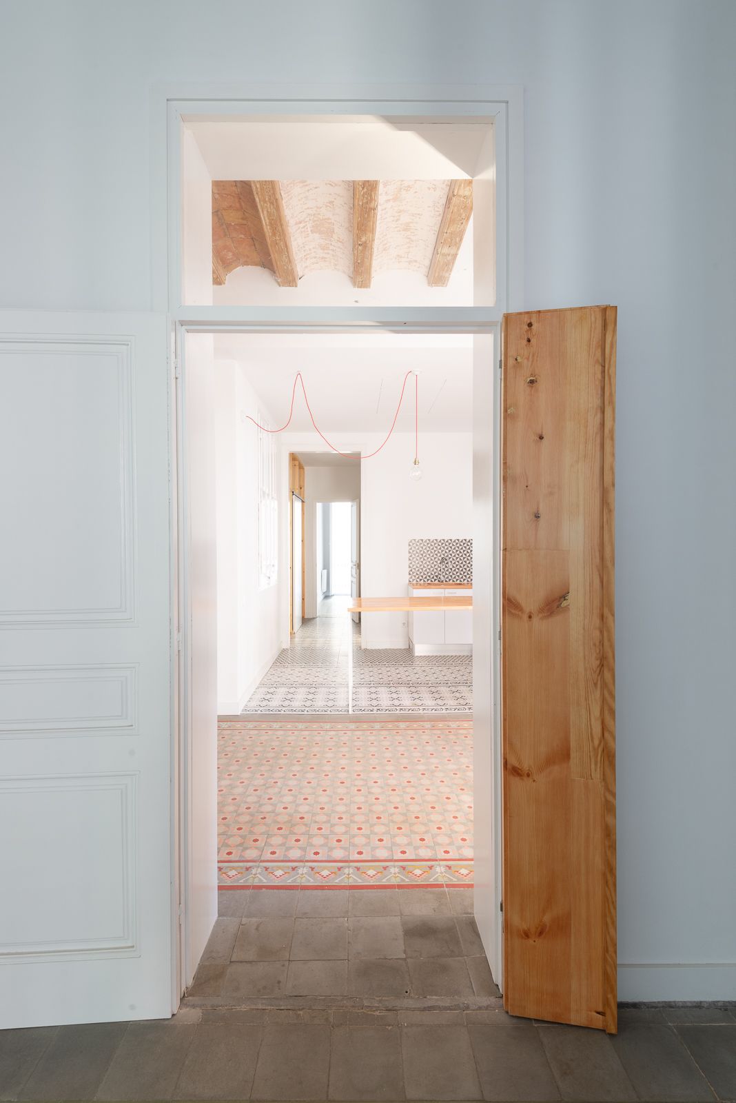 Open door revealing a room with patterned floor tiles and exposed wooden beams on the ceiling.