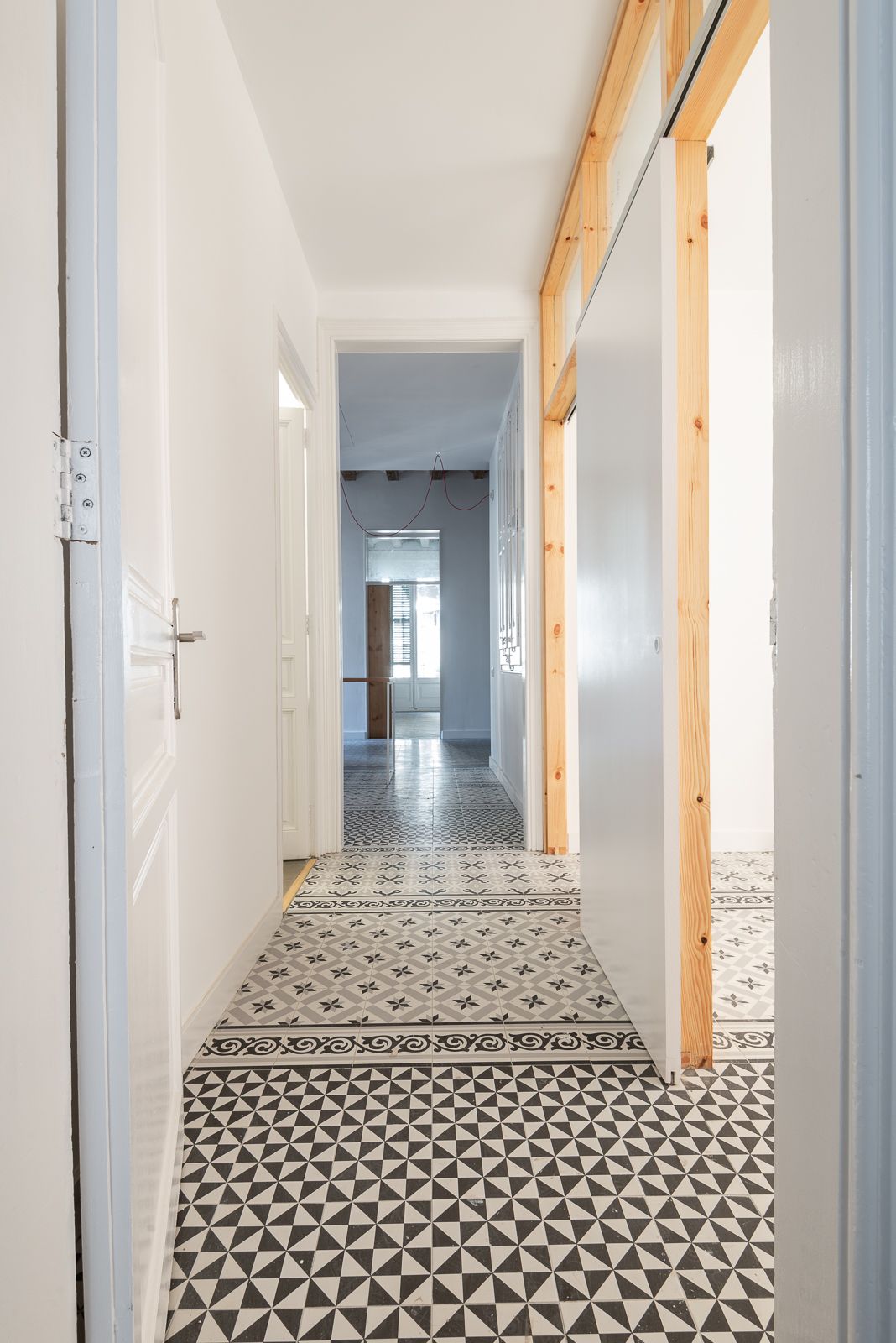Hallway with patterned floor tiles and a wooden frame leading to a bright room.