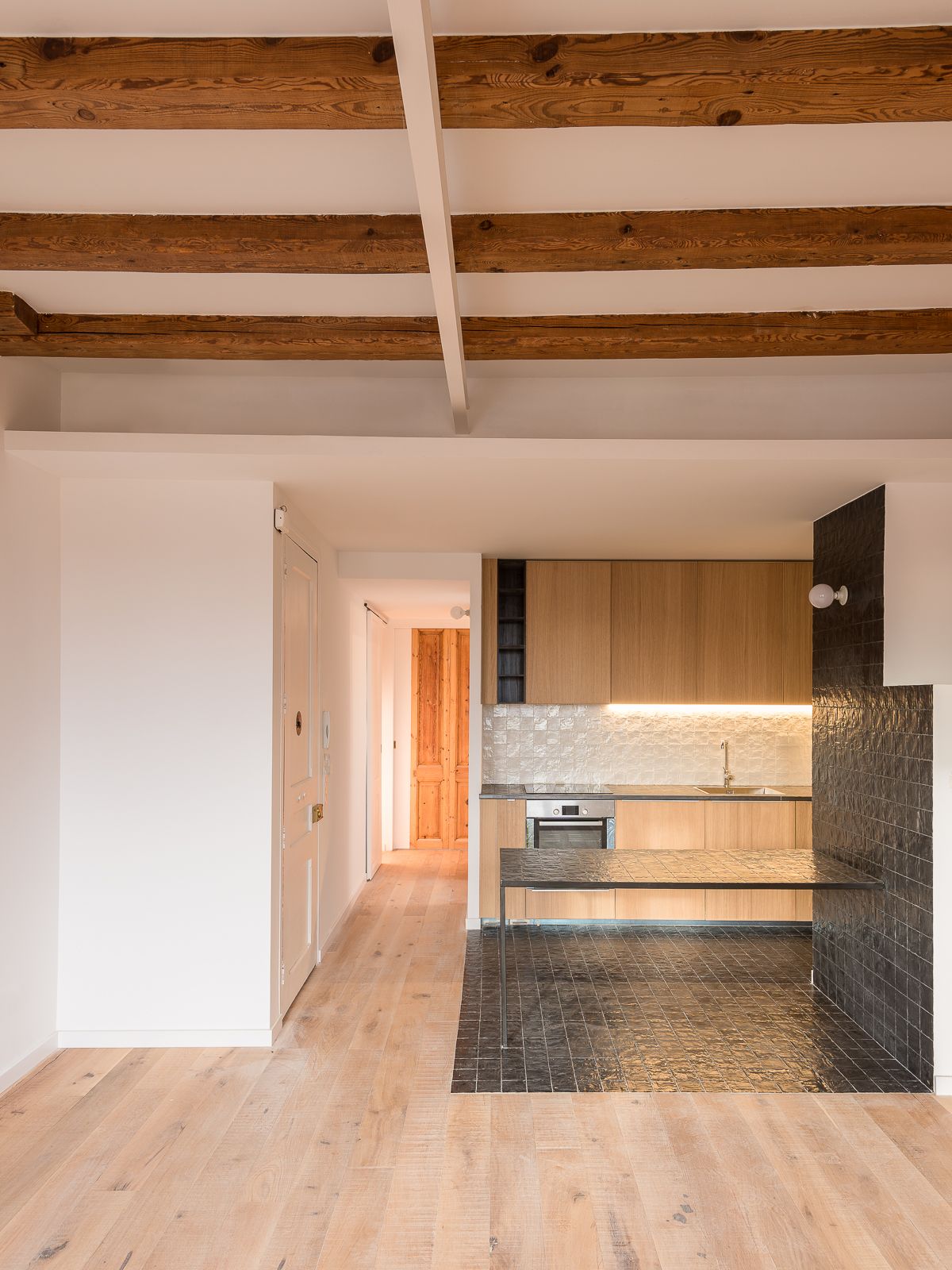 Open kitchen with wooden cabinets, black tiled countertop, and wooden beams on the ceiling.