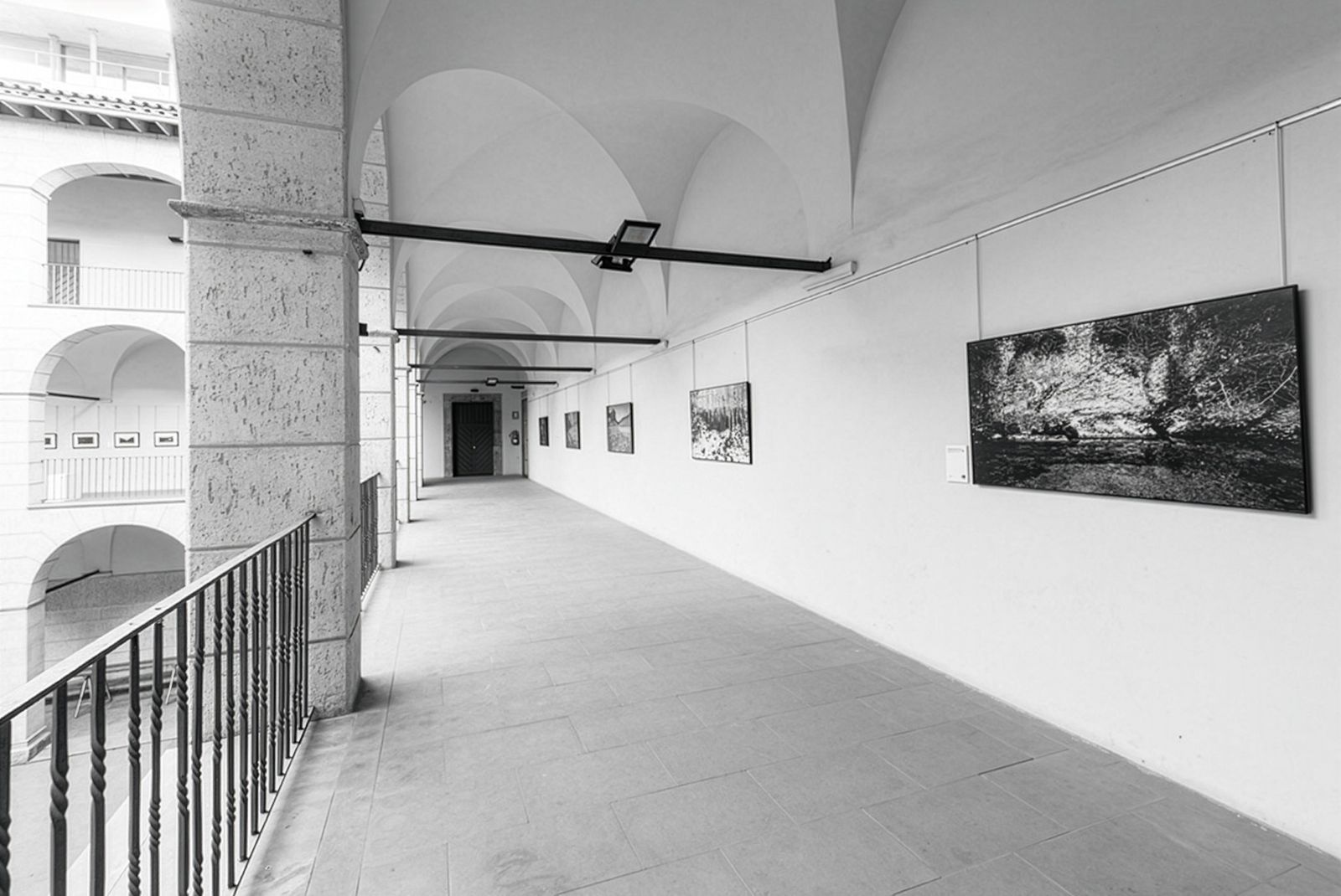 Covered walkway in an art gallery with photographs displayed on the walls.