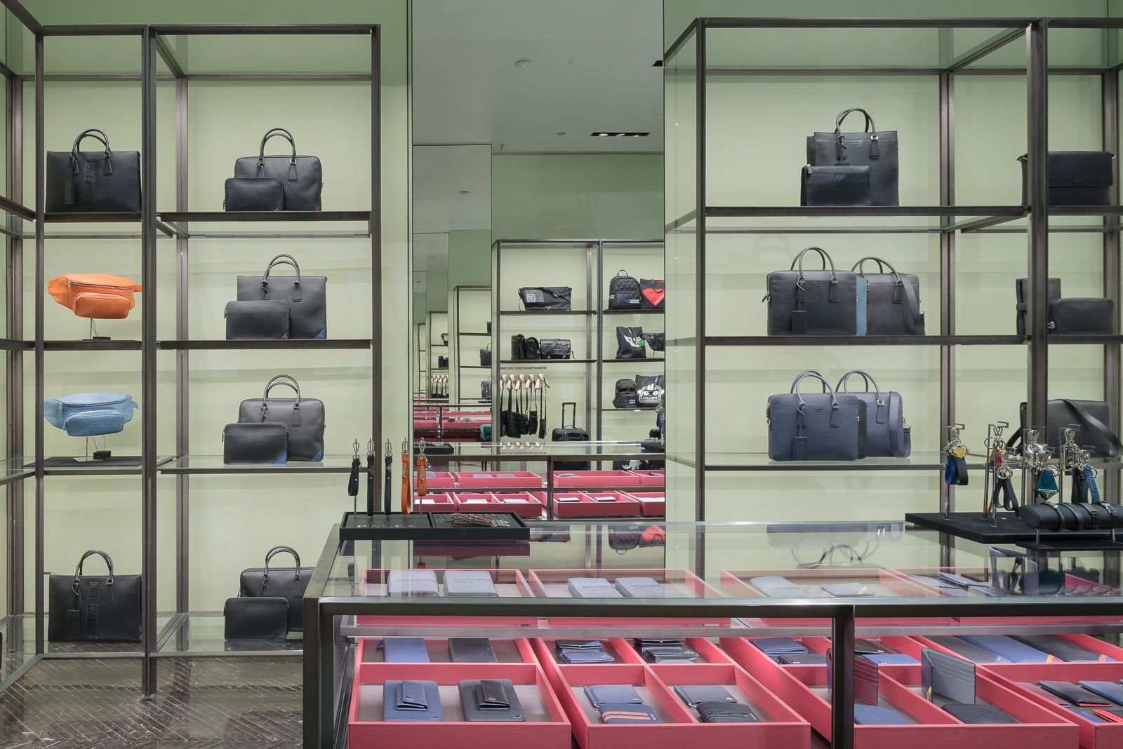 Prada store interior with two facing mirrors featuring an infinity mirror effect, there are shelves of designer bags in various colors, organized neatly against a light green background.